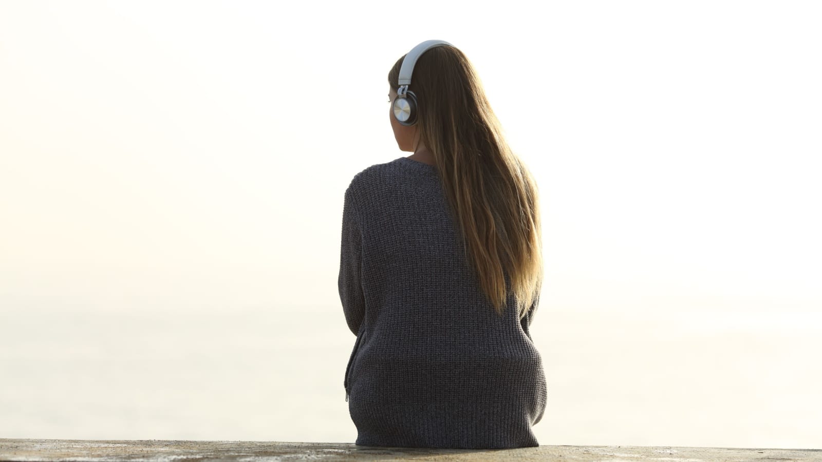 Back view of a woman sitting outside wearing headphones.