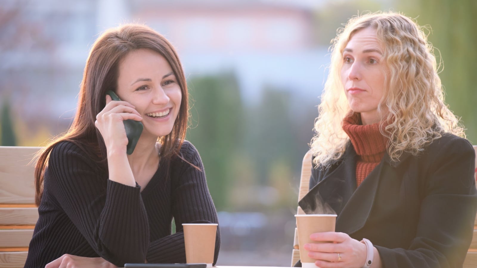 A woman ignores her friend, instead talking on the phone while her friend looks sad and bored.