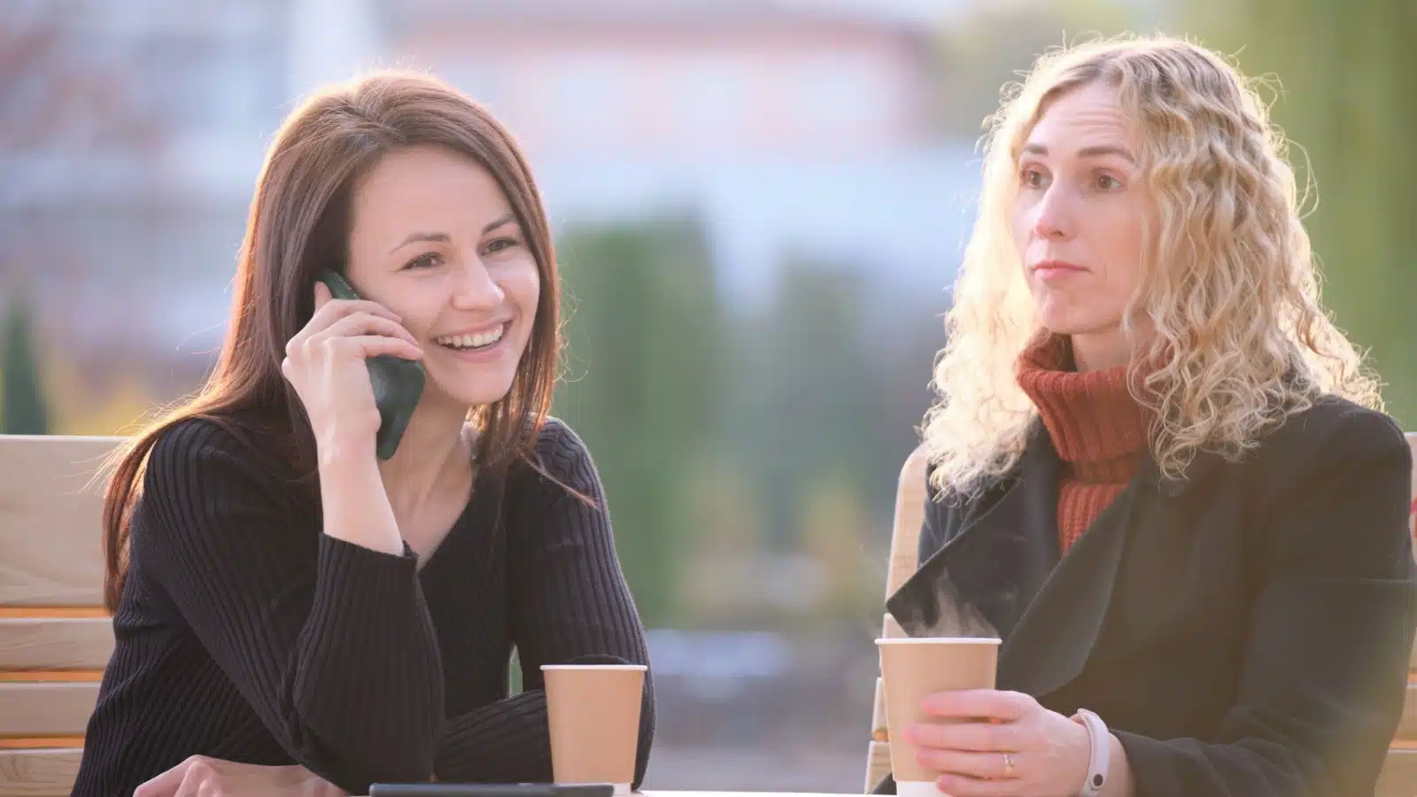 A woman ignores her friend, instead talking on the phone while her friend looks sad and bored.