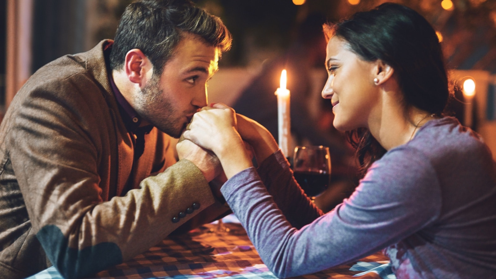 A couple at a romantic dinner. The man is holding her hands and staring into her eyes to represent creepy dating behaviors.