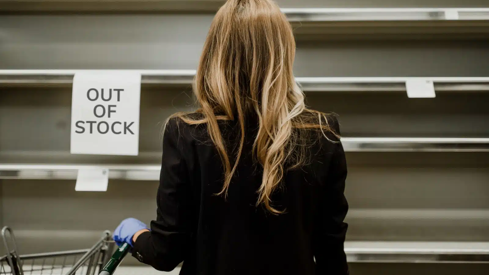 A woman looking at empty shelves at the grocery store to represent fake scarcity.