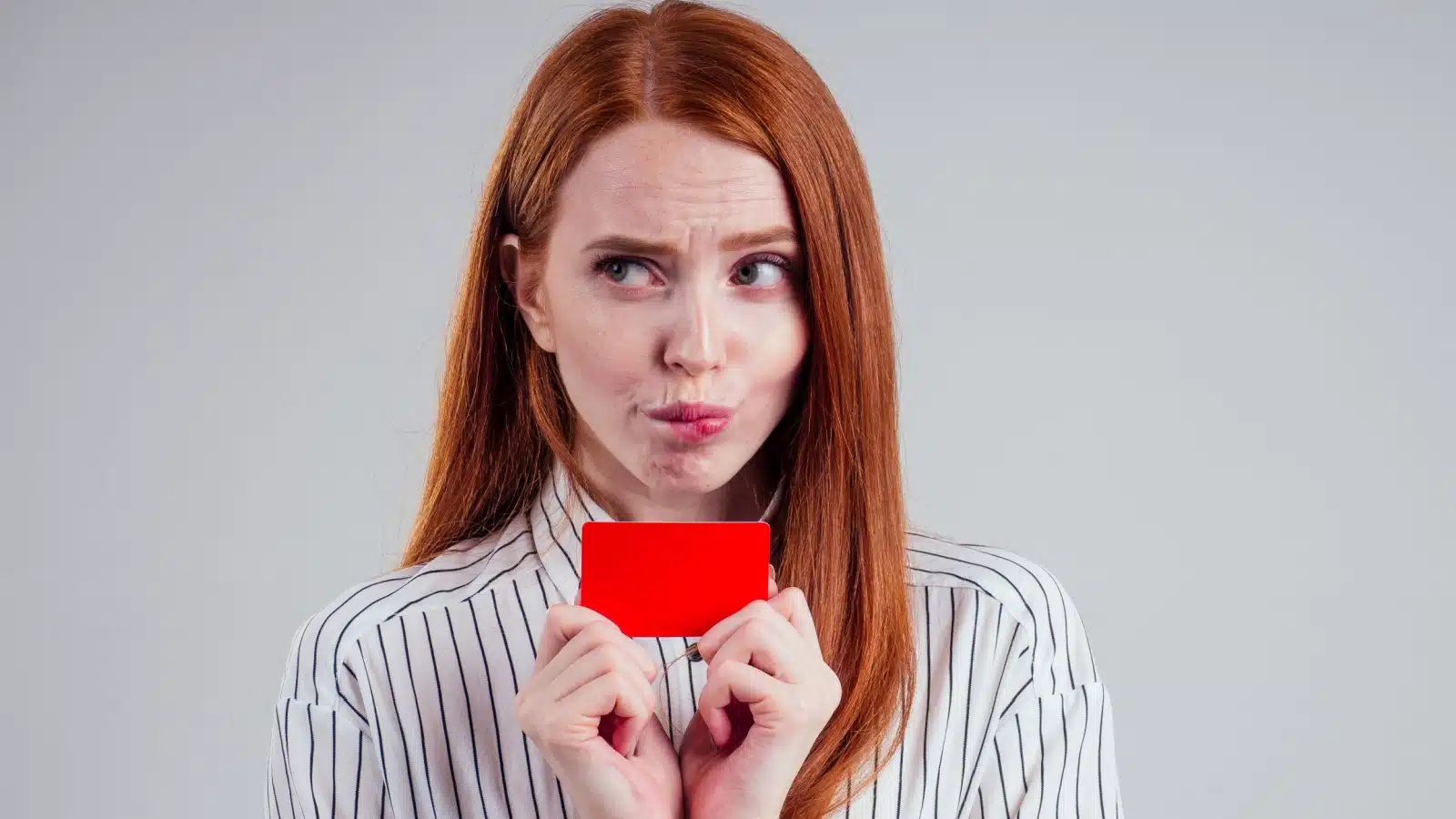 A woman holds her credit card, but she looks like she feels guilty for even thinking about spending money.