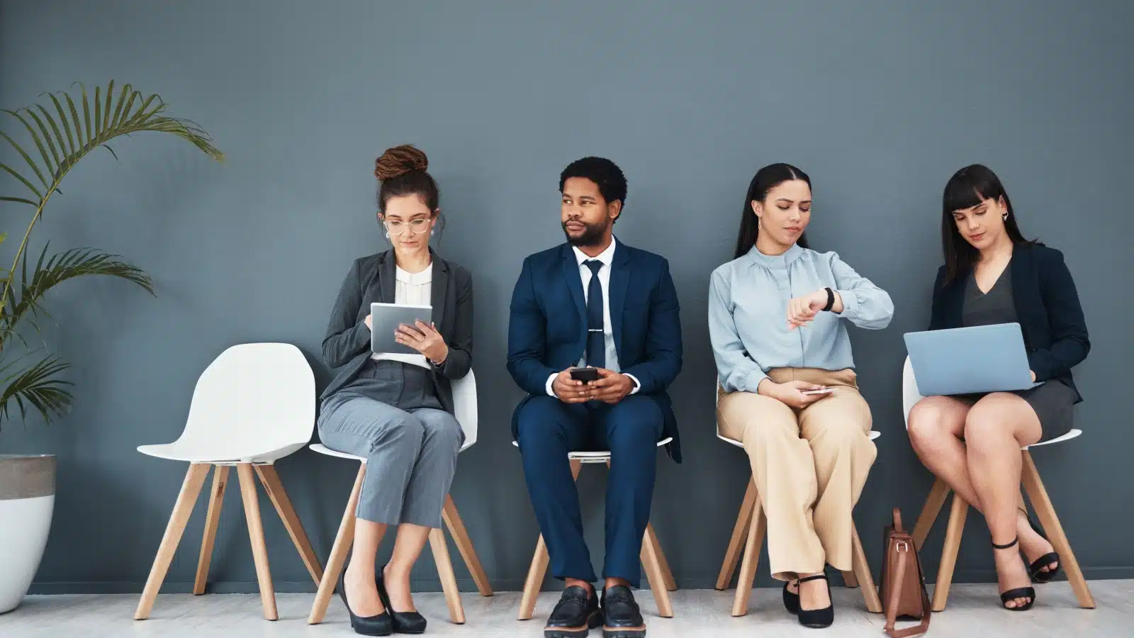 Job seekers waiting on chairs in a lobby to represent how long should you wait for an interview. 