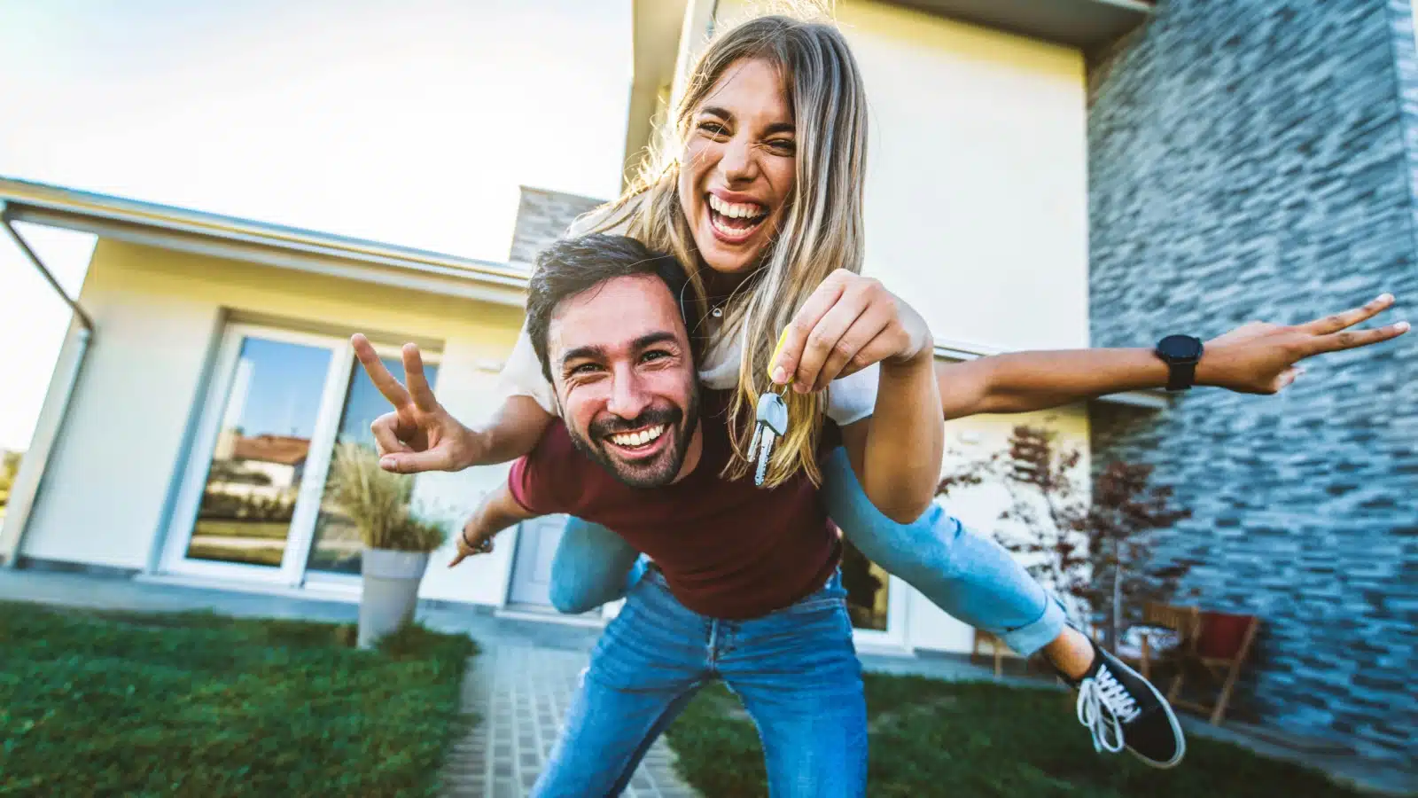 A happy, excited couple outside their new home showing off the keys to represent impulse buying a house.