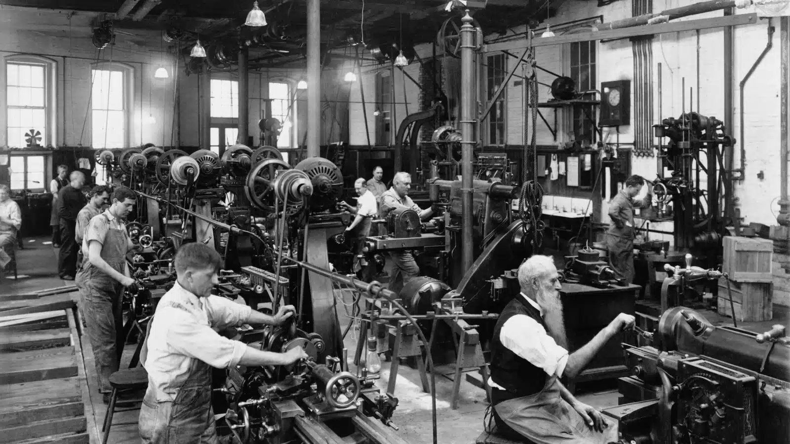 Black & white historical photo of men working at machines in DC to represent the Industrial Revolution. 