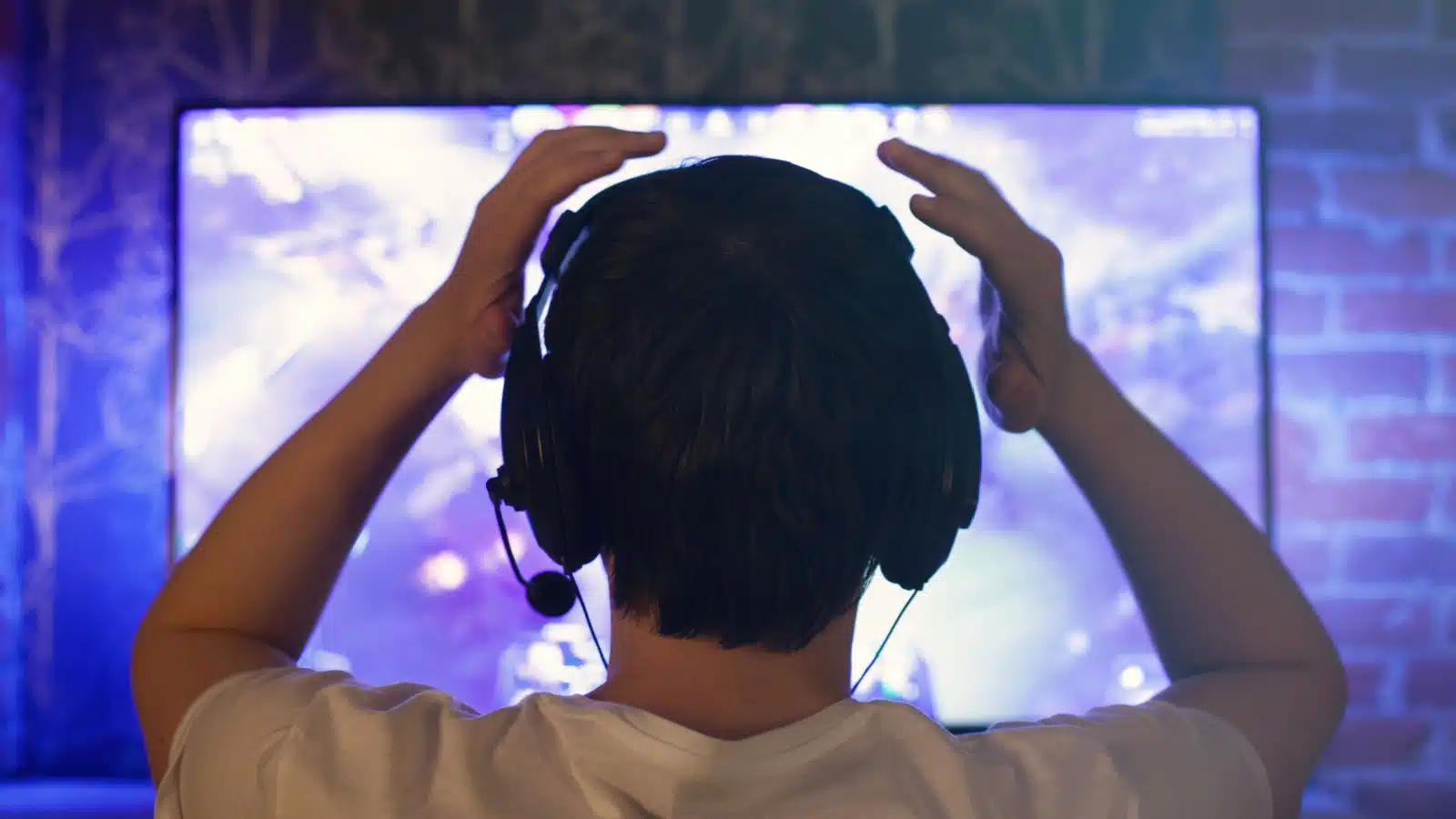 Back view of a gamer with his hands on his head after losing in a video game.