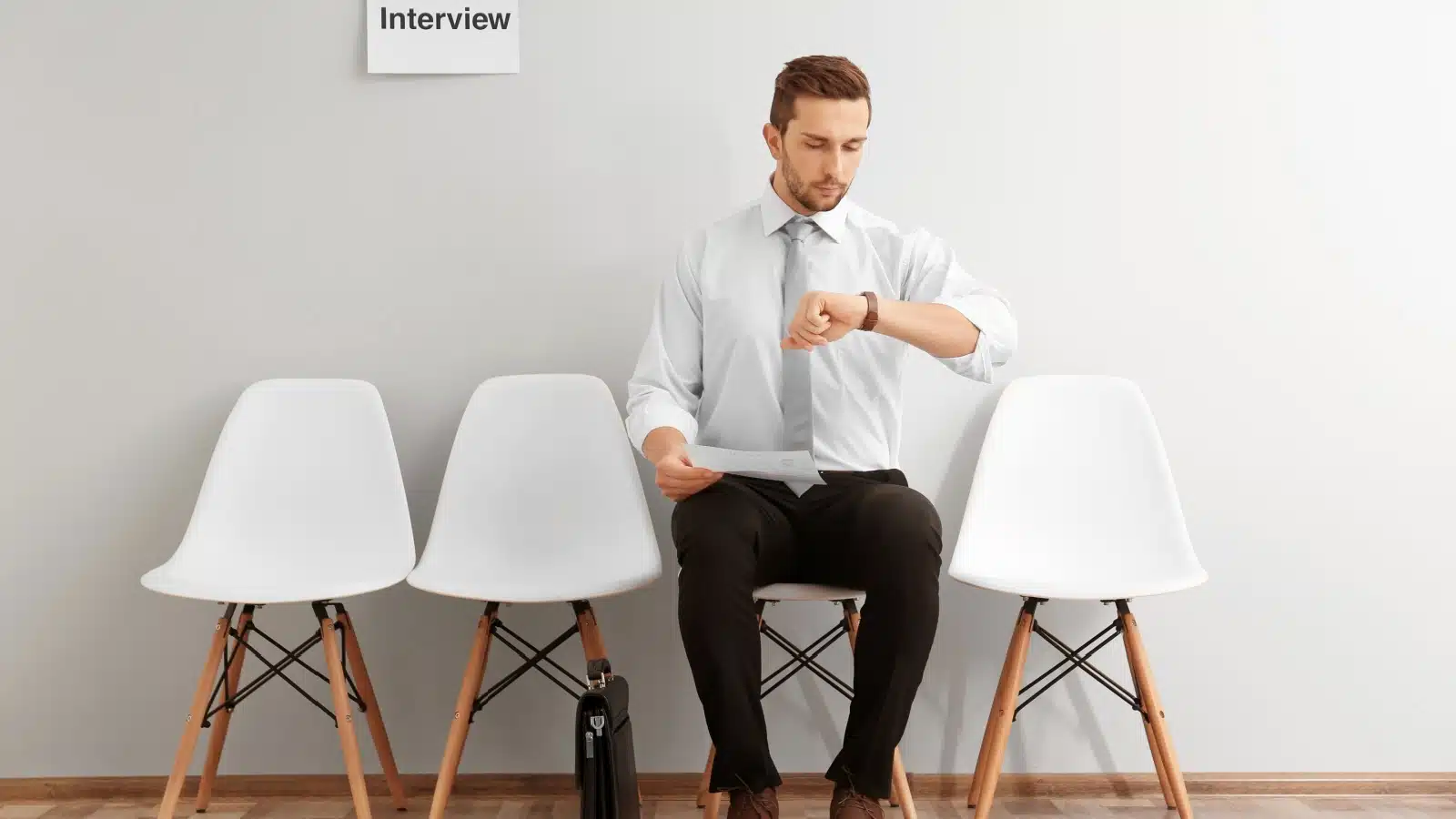 A man sits alone in an interview lobby, checking his watch as he waits for his interview. 