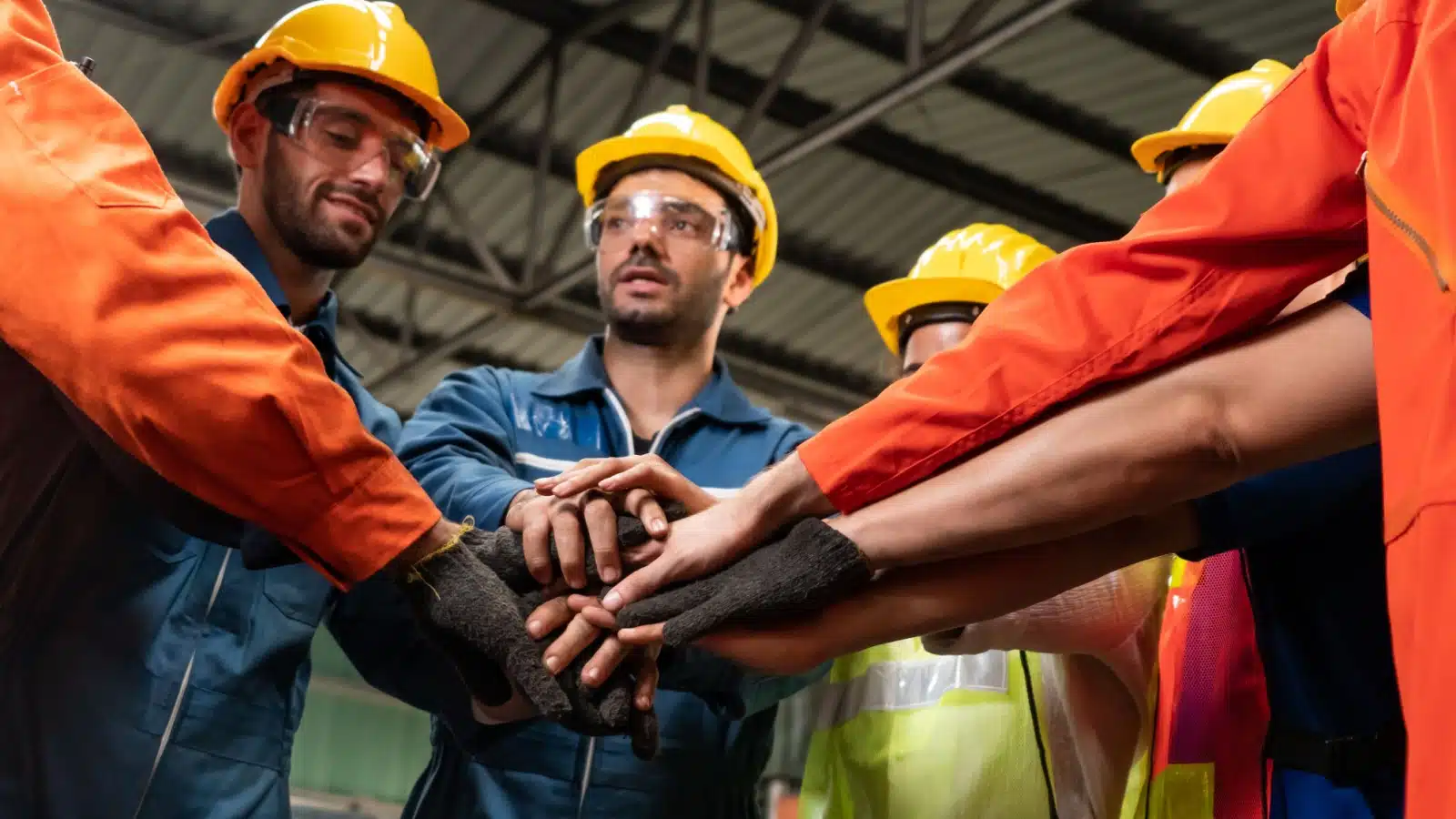 A group of workers stands together putting their hands together in a show of solidarity to represent a worker's union or labor union.