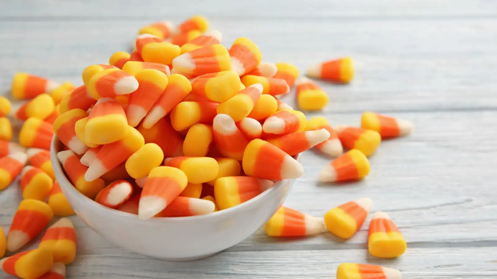 A bowl so full of candy corn it's spilling out on the table.
