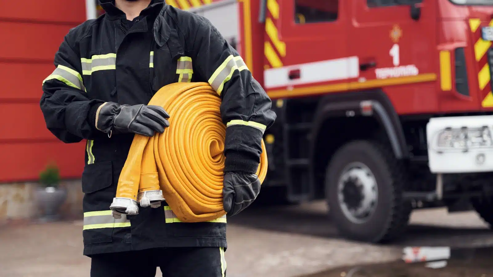 A fire fighter holds a hose in front of a fire truck.