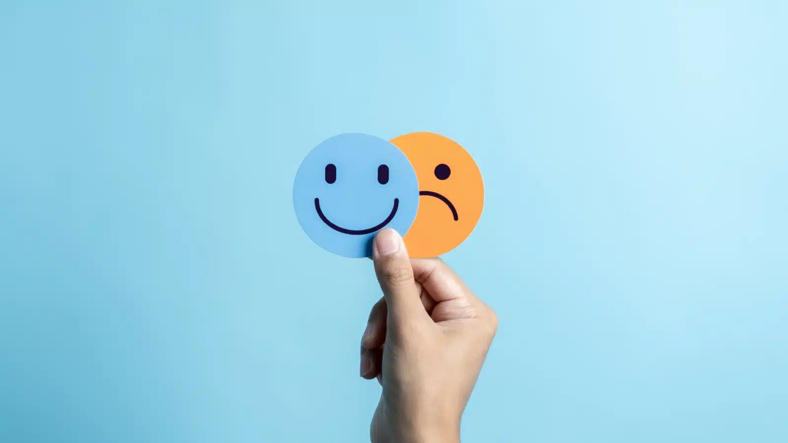 A hand holding up emojis representing happiness and sadness.