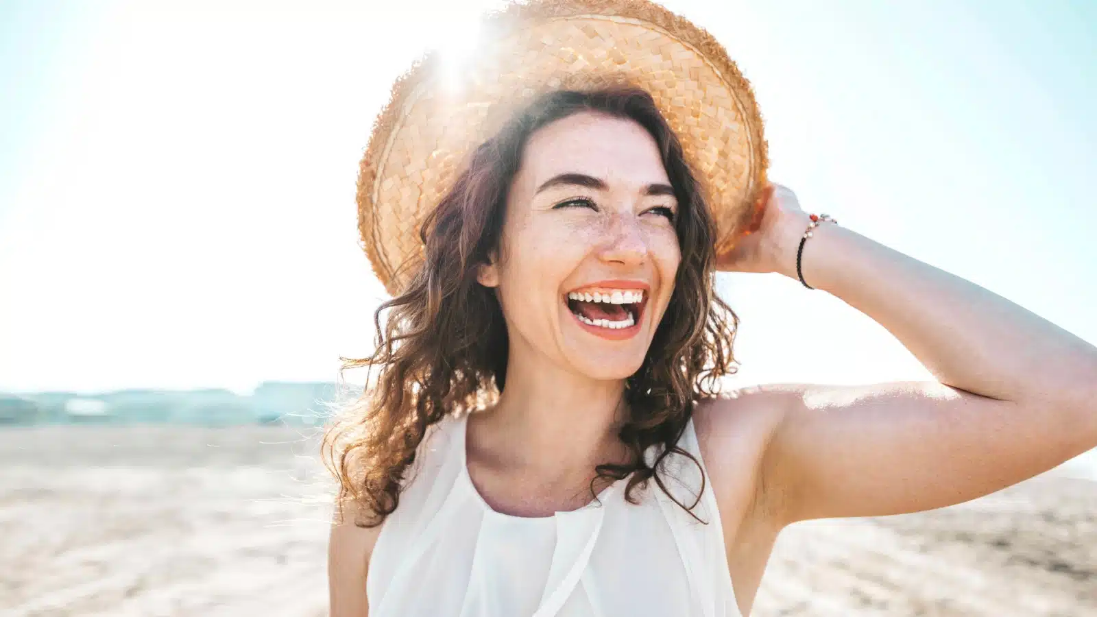 A woman at the beach wears a huge smile. She represents how to be happy.