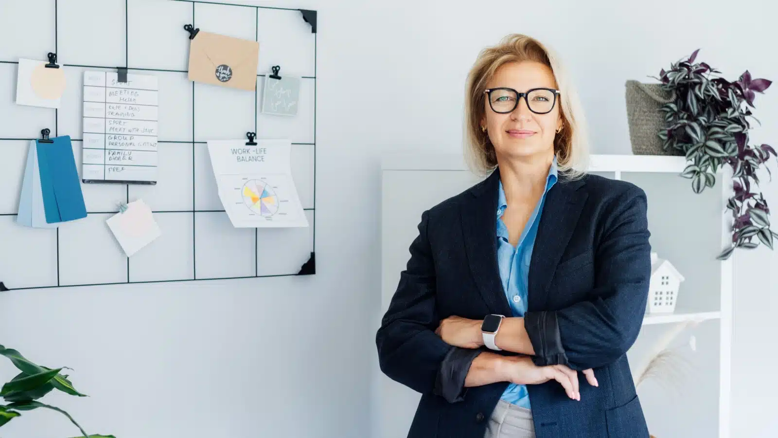 A smiling middle aged woman stands in front of a white board with imagery of work life balance on it to represent how to improve your life.