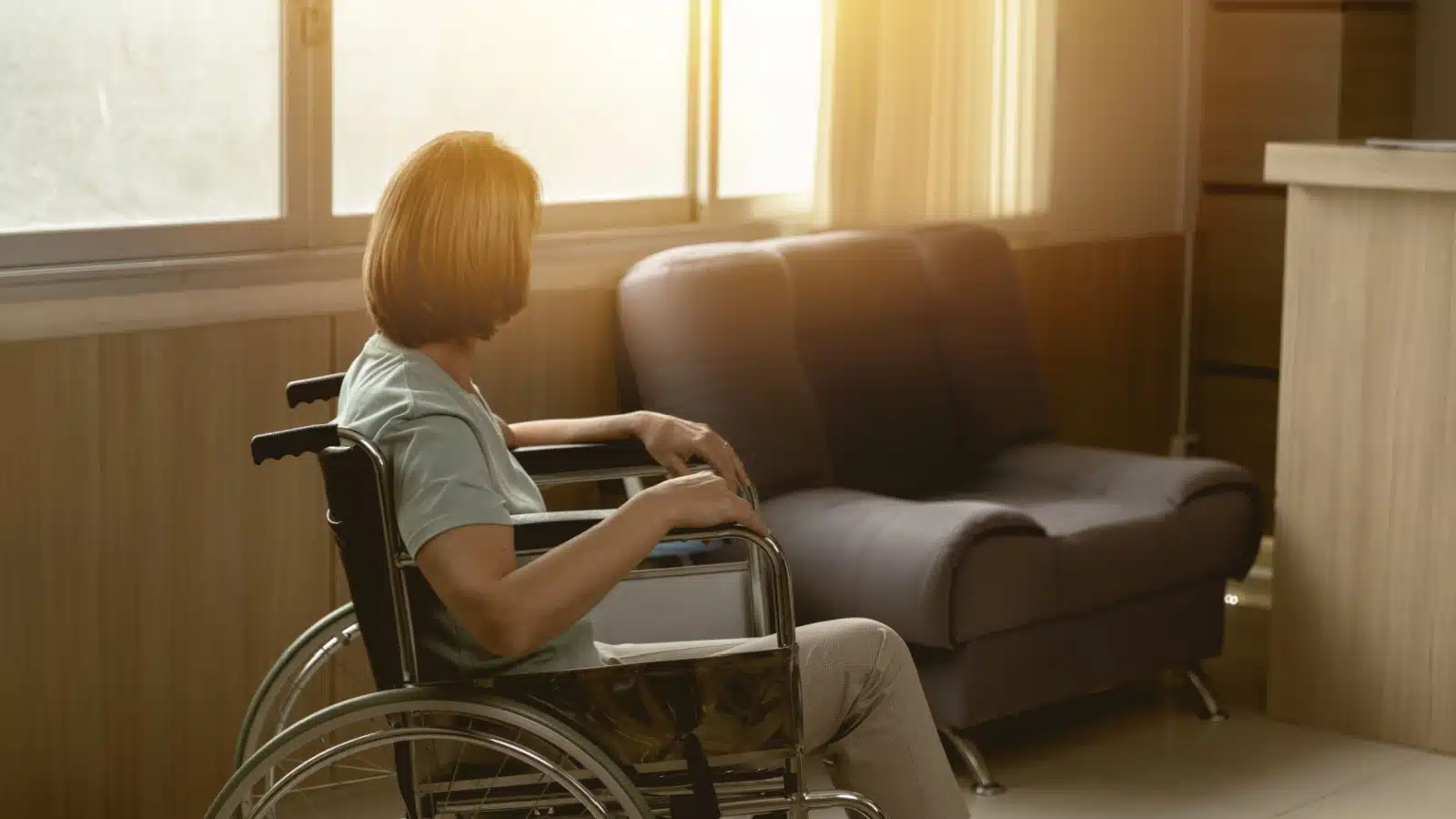 A sick woman sits alone in a wheelchair, looking at the empty chair. The image represents that sad truth that men leave their sick wives at high rates.