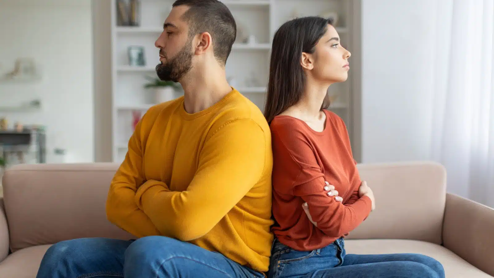 A man and woman sit back-to-back on the couch, mirroring each other's anger. It represents how to match his energy.