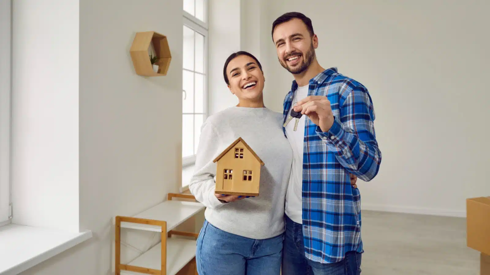 A couple holds keys and a model house to represent home ownership.