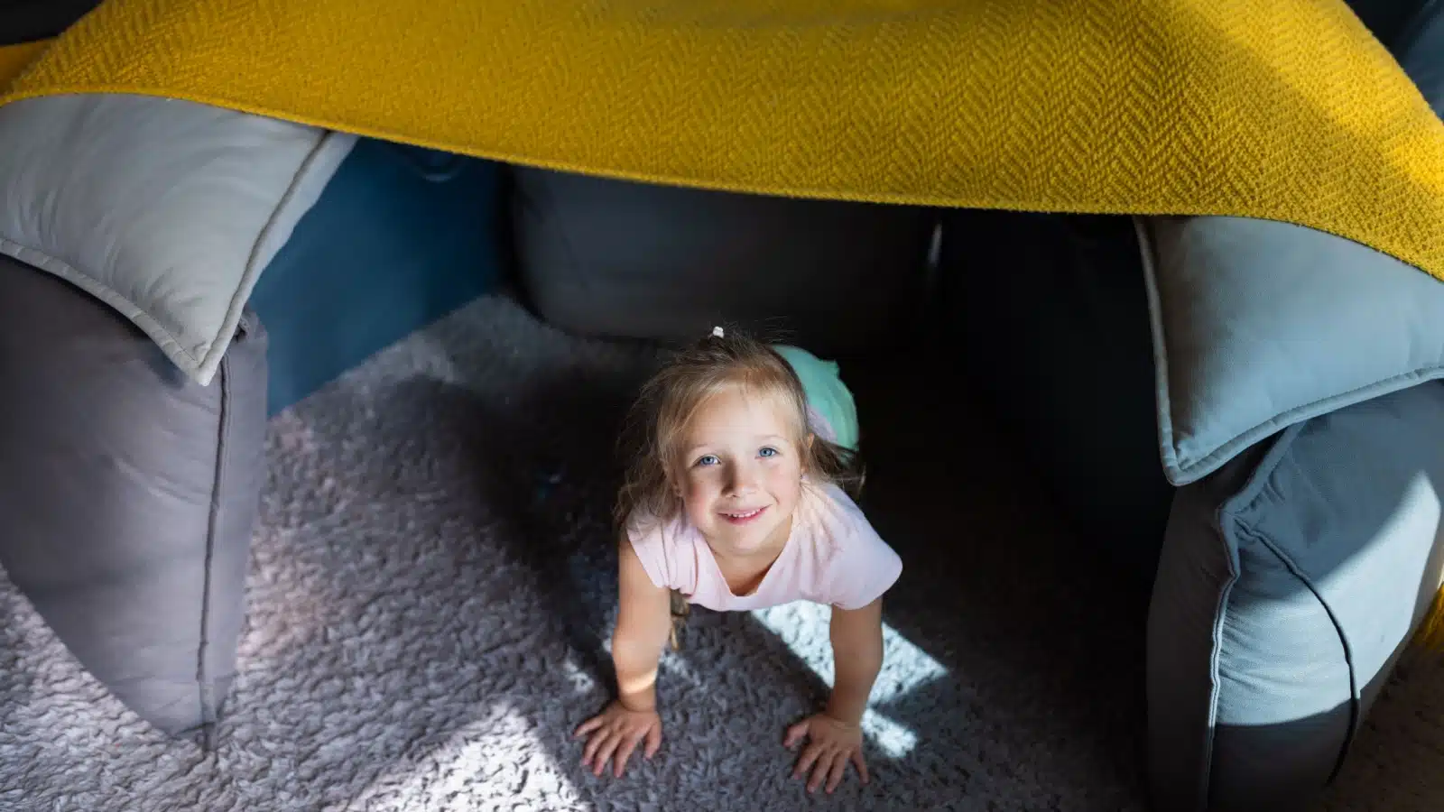 A little girl plays in a cushion fort.