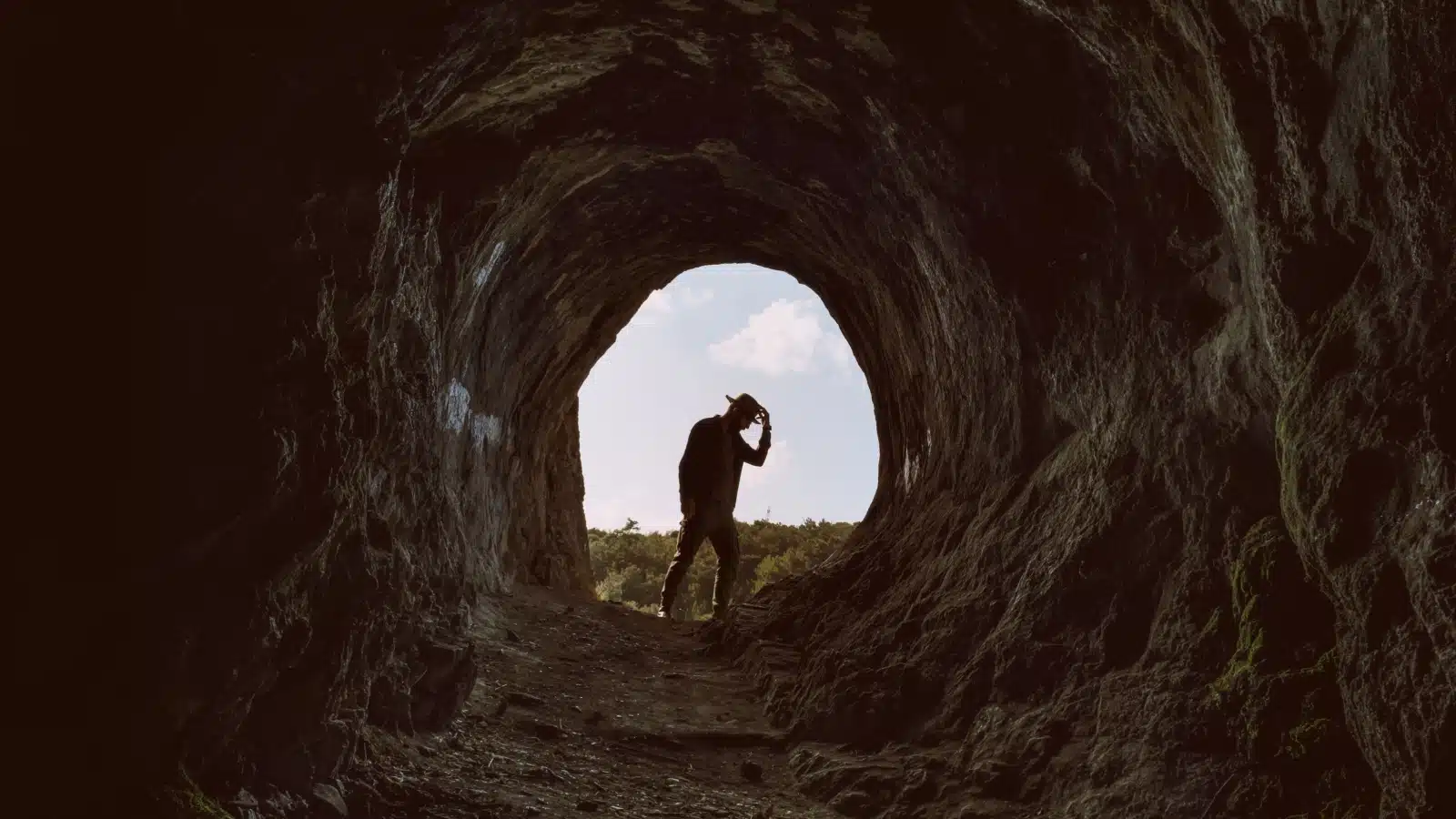 Image of a man wearing a hat at the mouth of a cave, in the style of Indiana Jones in Raiders of the Lost Ark, to represent a Hero's journey. 