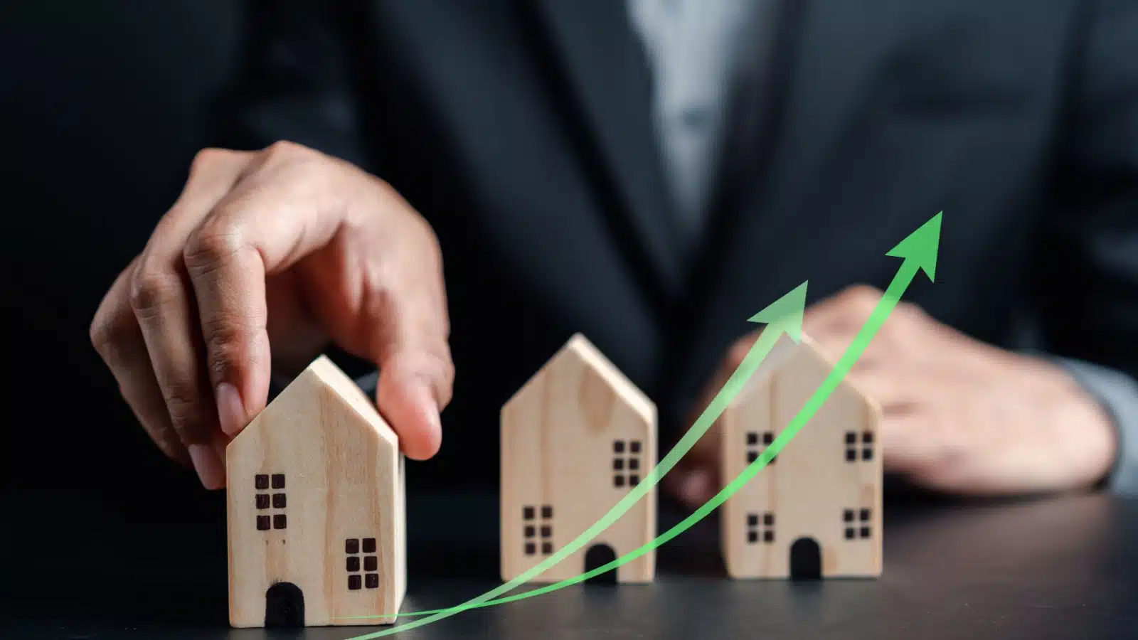 A business man setting up miniature block houses with a green upward arrow running through them to represent the truth about real estate investing.