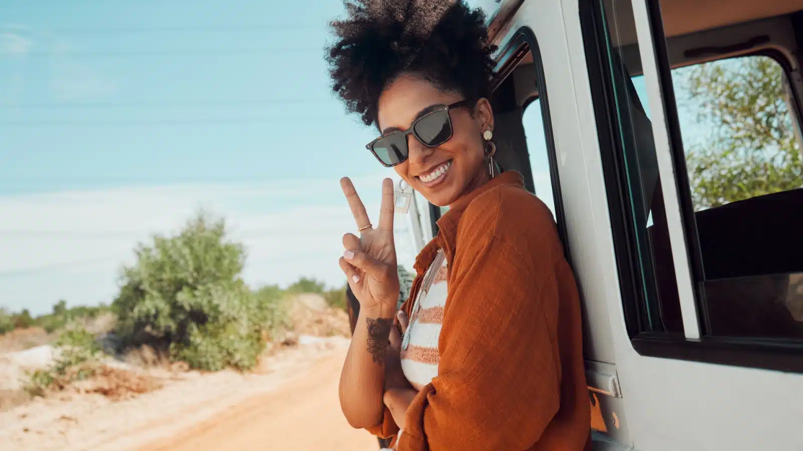 A happy woman stands outside her van, enjoying her life journey.