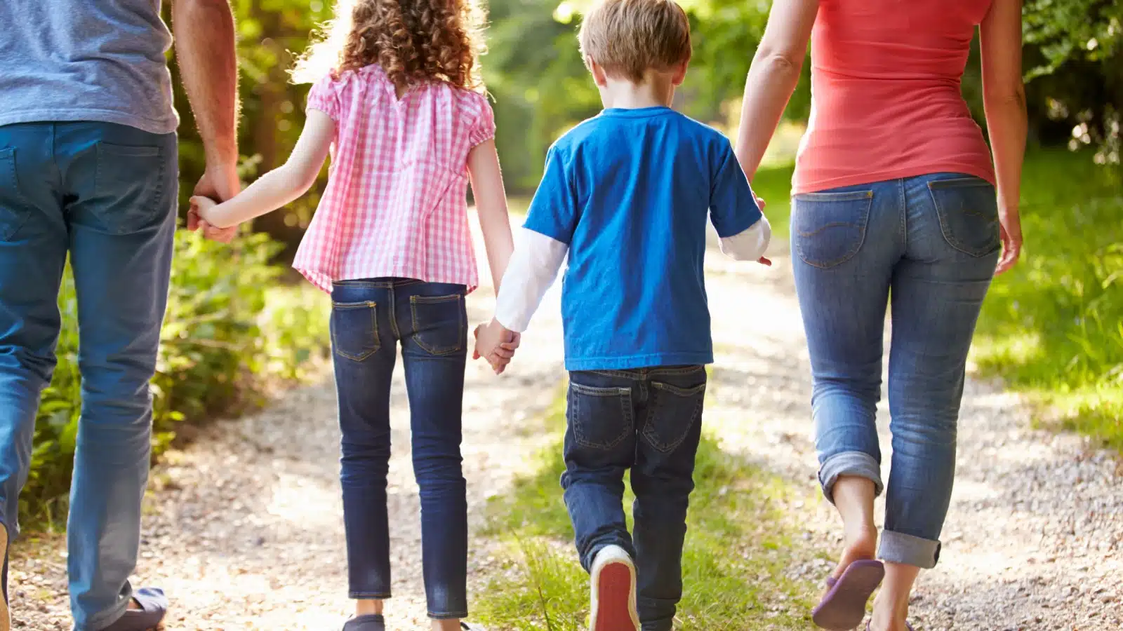 Rear view of a family of four which includes a mom, dad, son, and daughter, walking in the woods, to represent the question are boys or girls easier to raise.