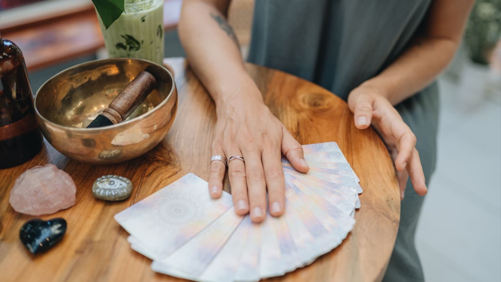 A woman spreads tarot cards on a table that also has crystals and a singing bowl to represent the eclectic witch.
