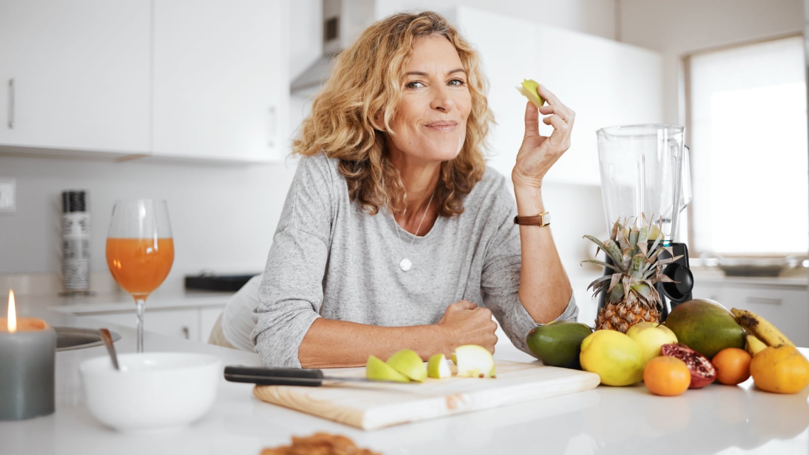 A healthy middle aged woman smiling as she eats fruit for breakfast in the morning to represent a happier, healthier you.
