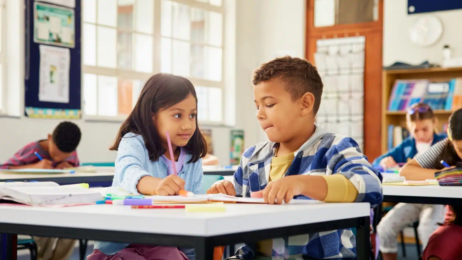 A little girl helps a little boy with his assignment in school.