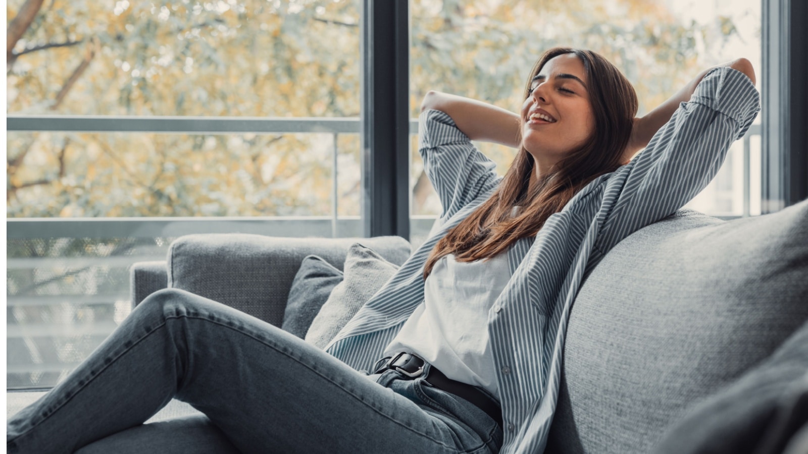 A happy woman relaxes on a couch to represent life hacks you can use for a simpler life.