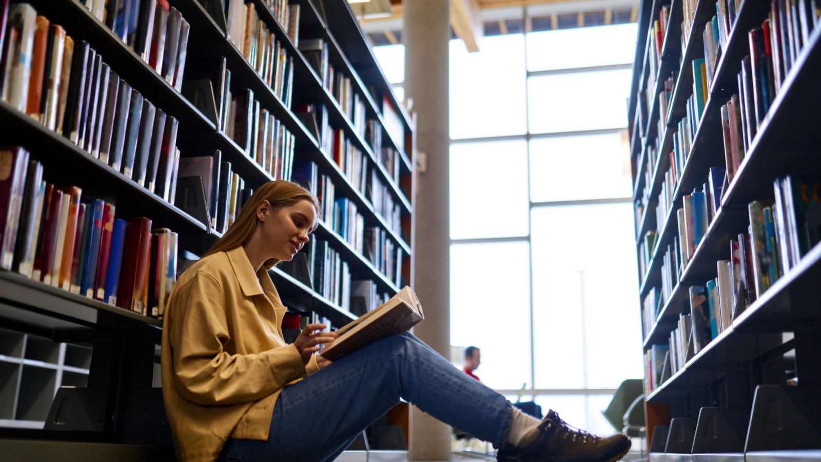 What is an introvert? A woman sits alone amongst the library shelves reading a book.