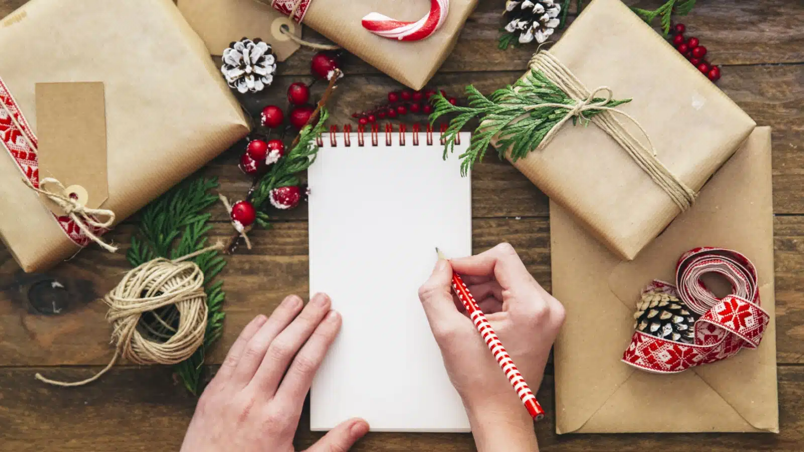 Writing a Christmas wish list on a desk surrounded by wrapped presents.
