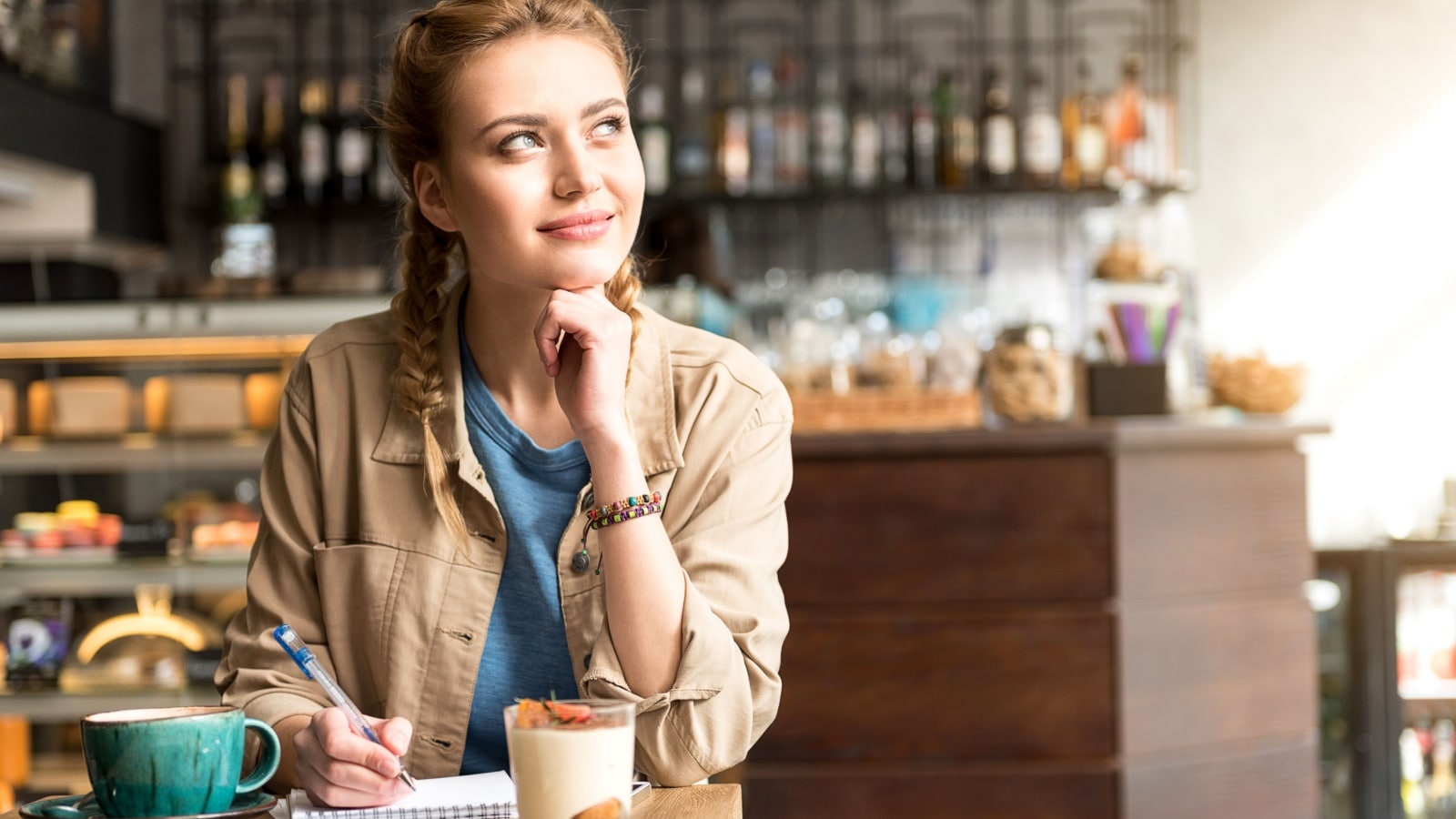 A woman thinking about how to make life better. She's in a coffee shop, happily thinking while writing a list.