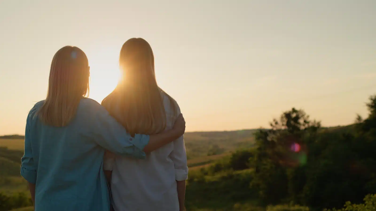 A mom hugs her teenage daughter as they watch the sunset together, to represent becoming an adult.
