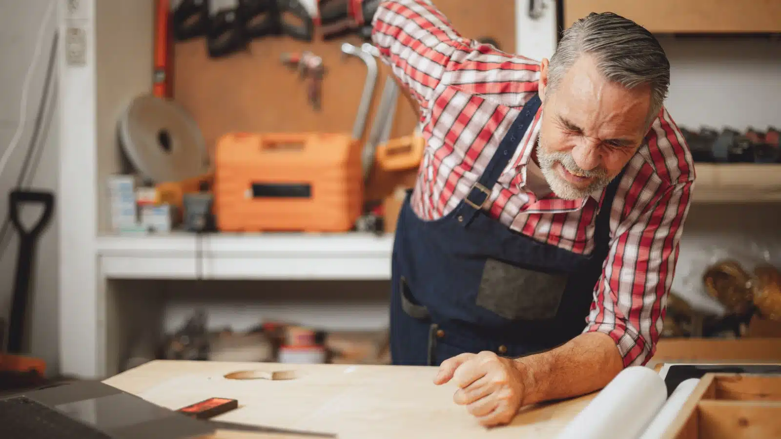 A senior worker leans over in pain at his work station.