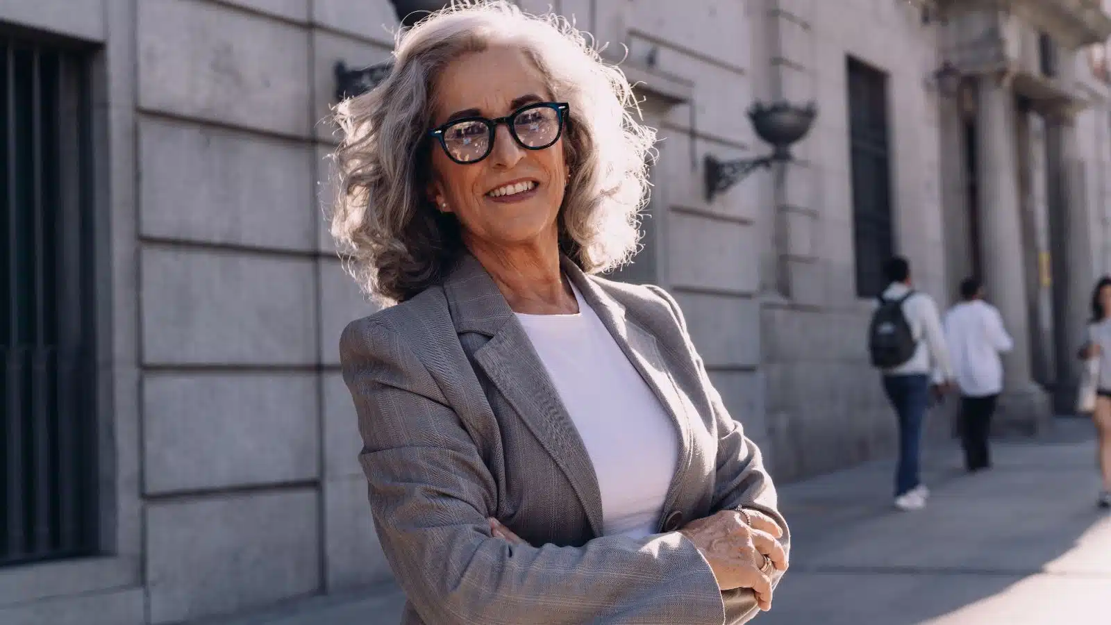 A successful independent senior businesswoman stands outside confidently with her arms crossed.