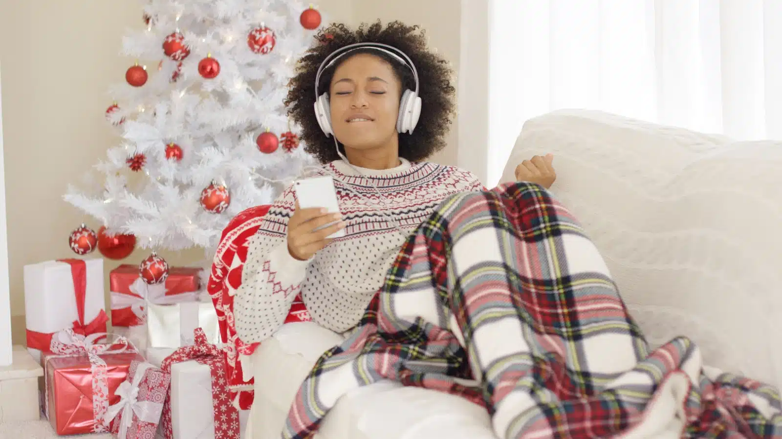 A woman surrounded by Christmas decor listens to music on her headphones.