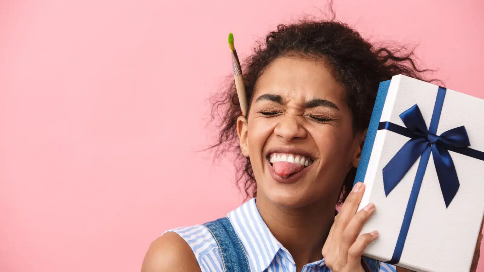 A woman with a paint brush tucked behind her ear is excited to receive a gift, to represent the best gifts for artists.