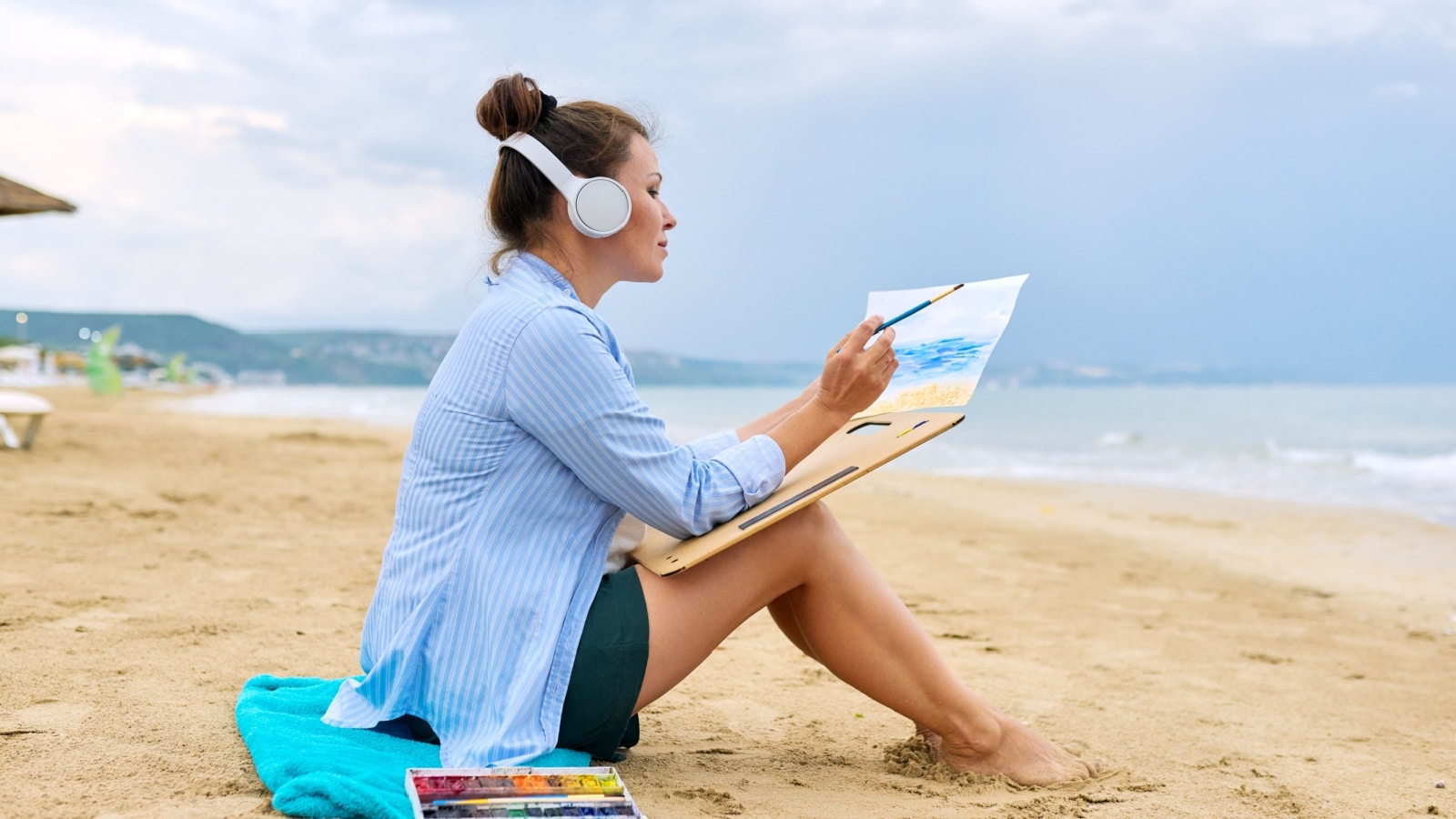 A woman paints in watercolors at the beach. 