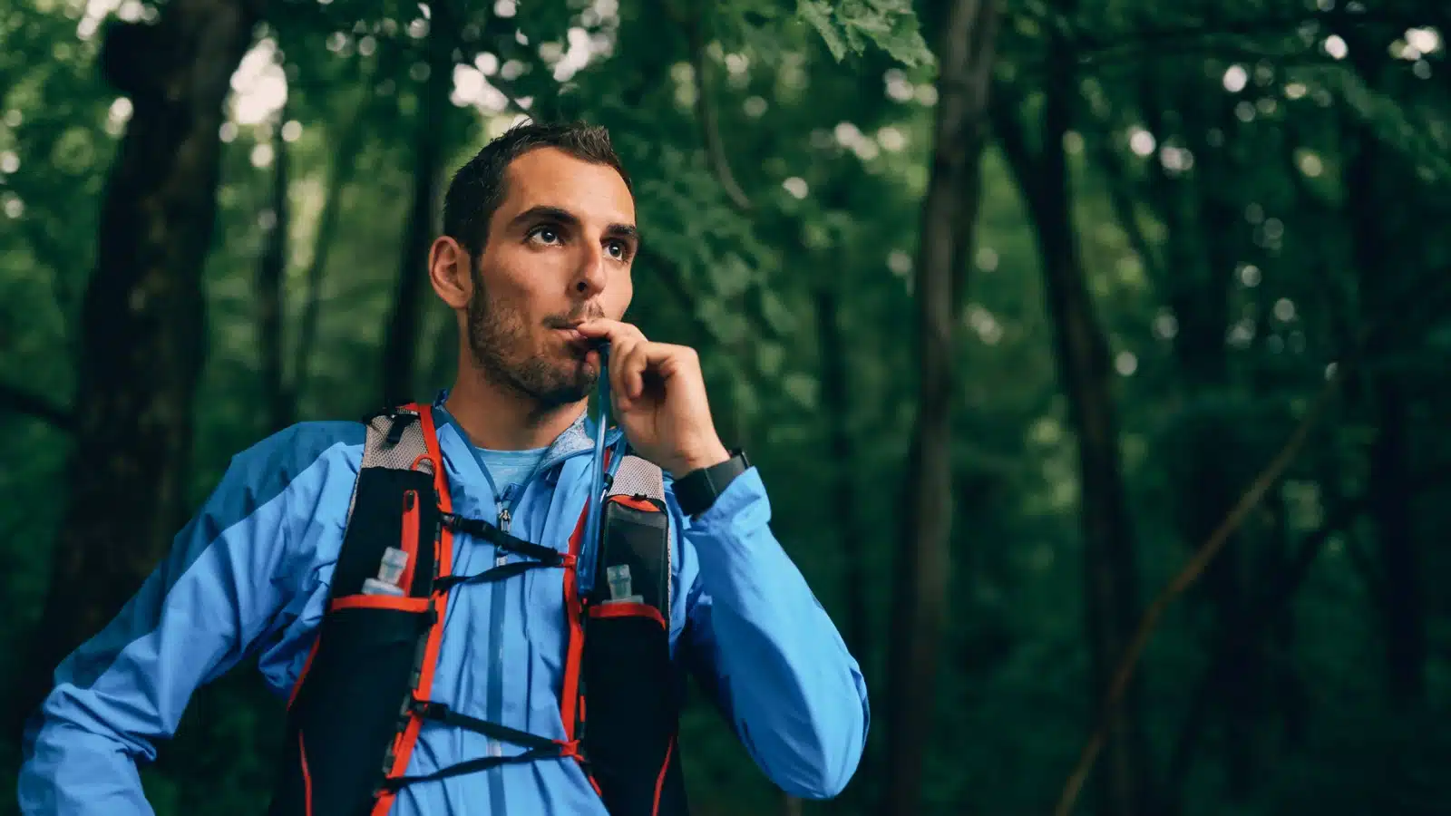A man drinking water from a hydration system backpack.