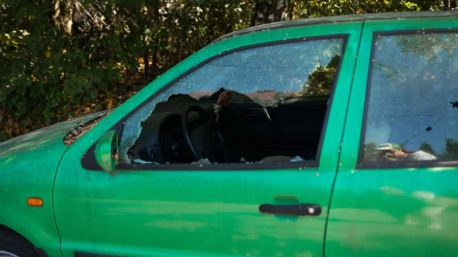A parked car with the front window smashed open so thieves could steal any valuables inside.