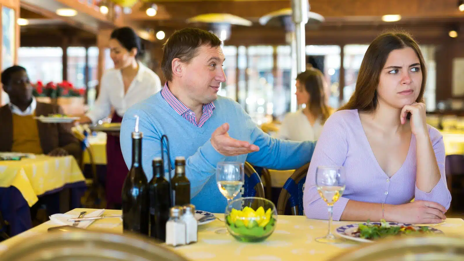A man looks like he's bargaining with his date, who looks away angrily to represent dating red flags.