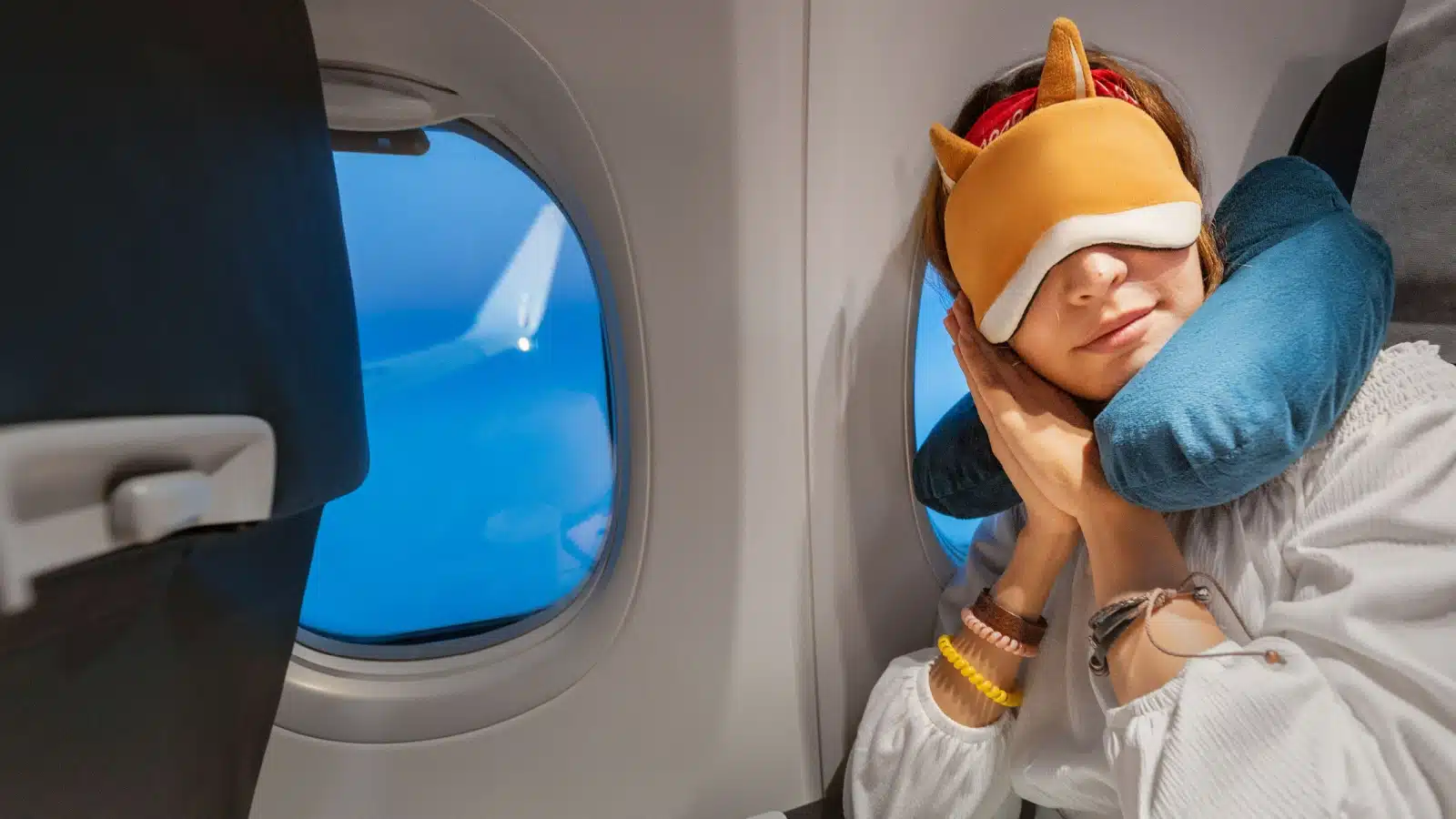 A woman sleeps on a flight with a neck pillow and eye mask.