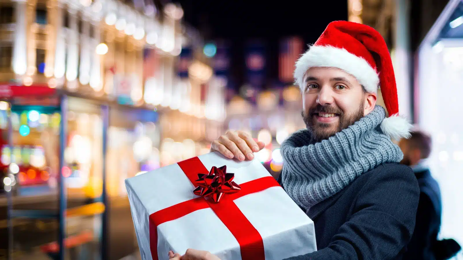 A tourist holding a giant gift standing outside a bright city around Christmas time to represent the best gifts for travelers.