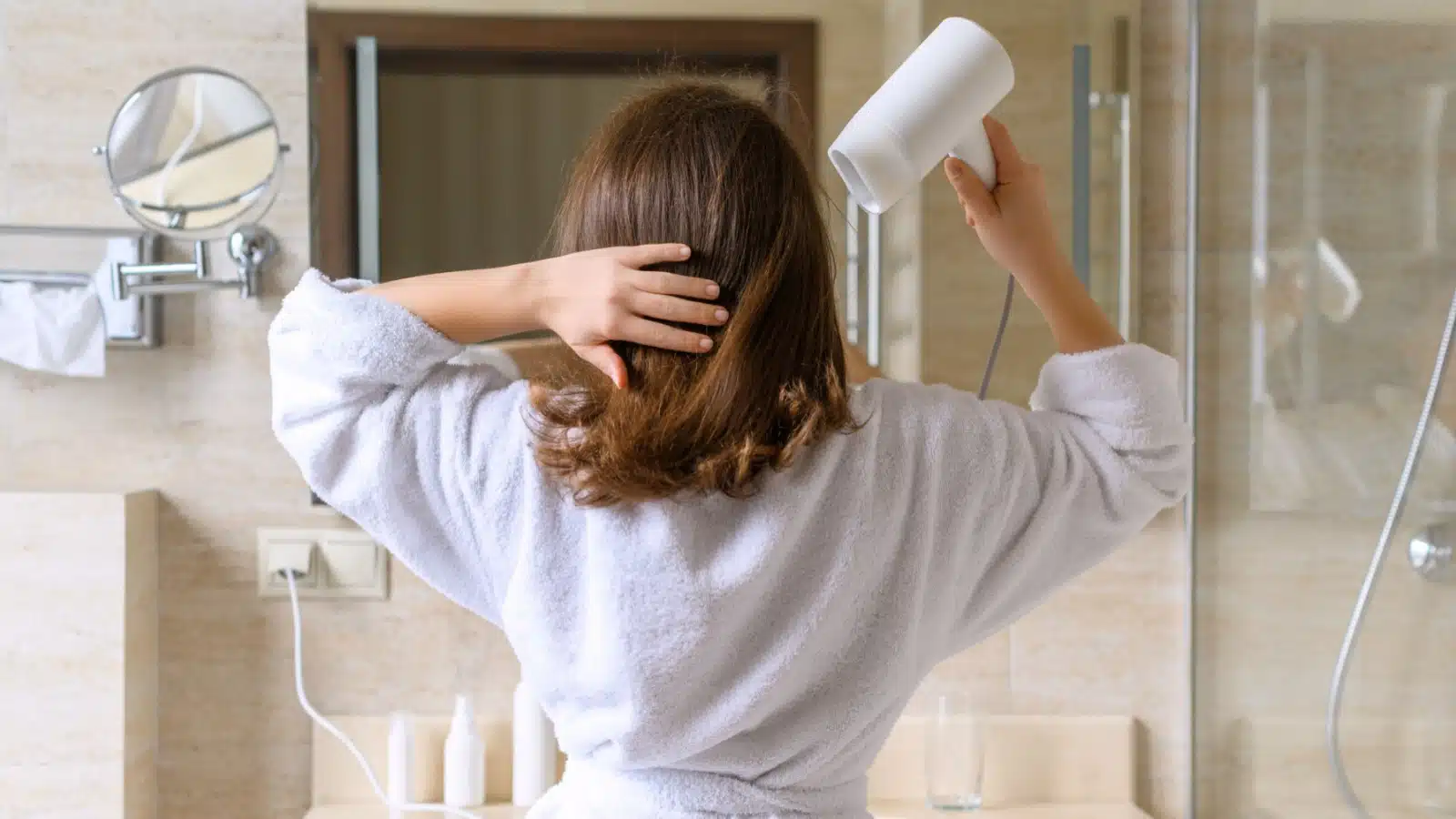 A woman in a bathroom drying her hair with a blow dryer.