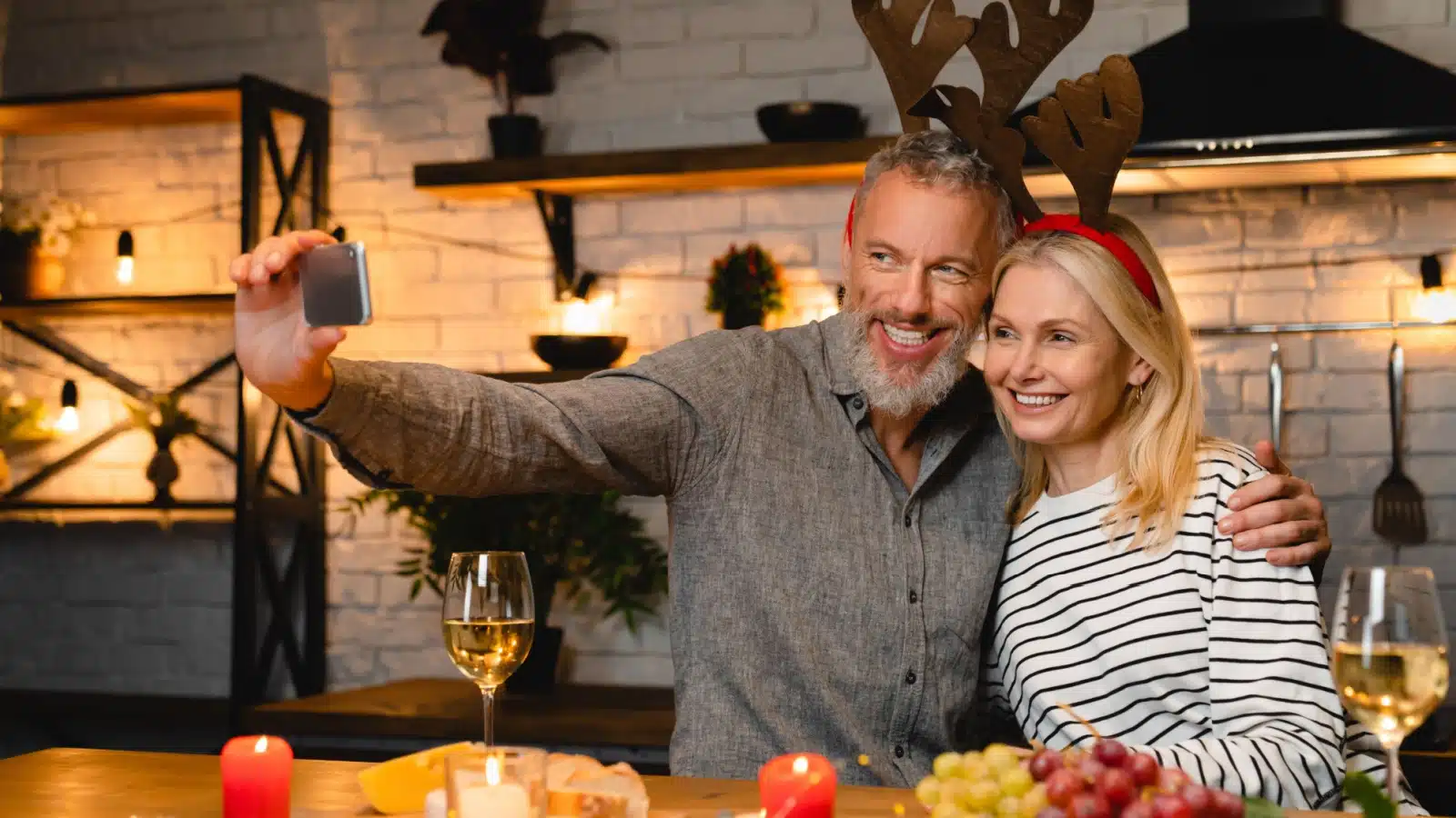 A happy couple takes a selfie before Christmas. They are wearing fake reindeer antlers as they celebrate the holiday season.