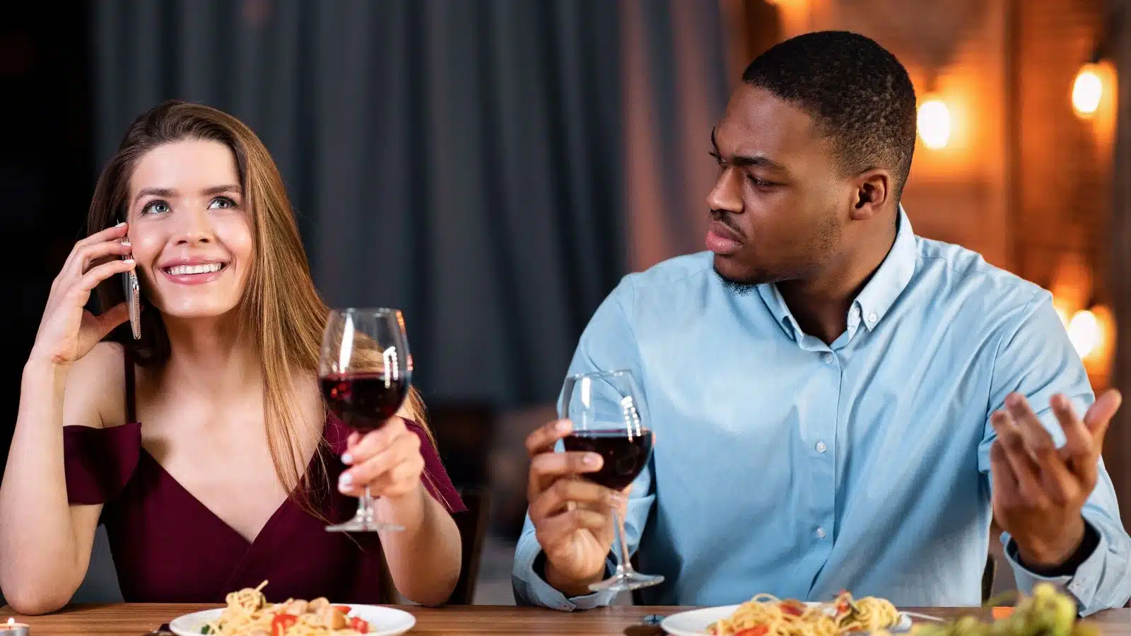 A woman chats on the phone ignoring her date, who looks upset.