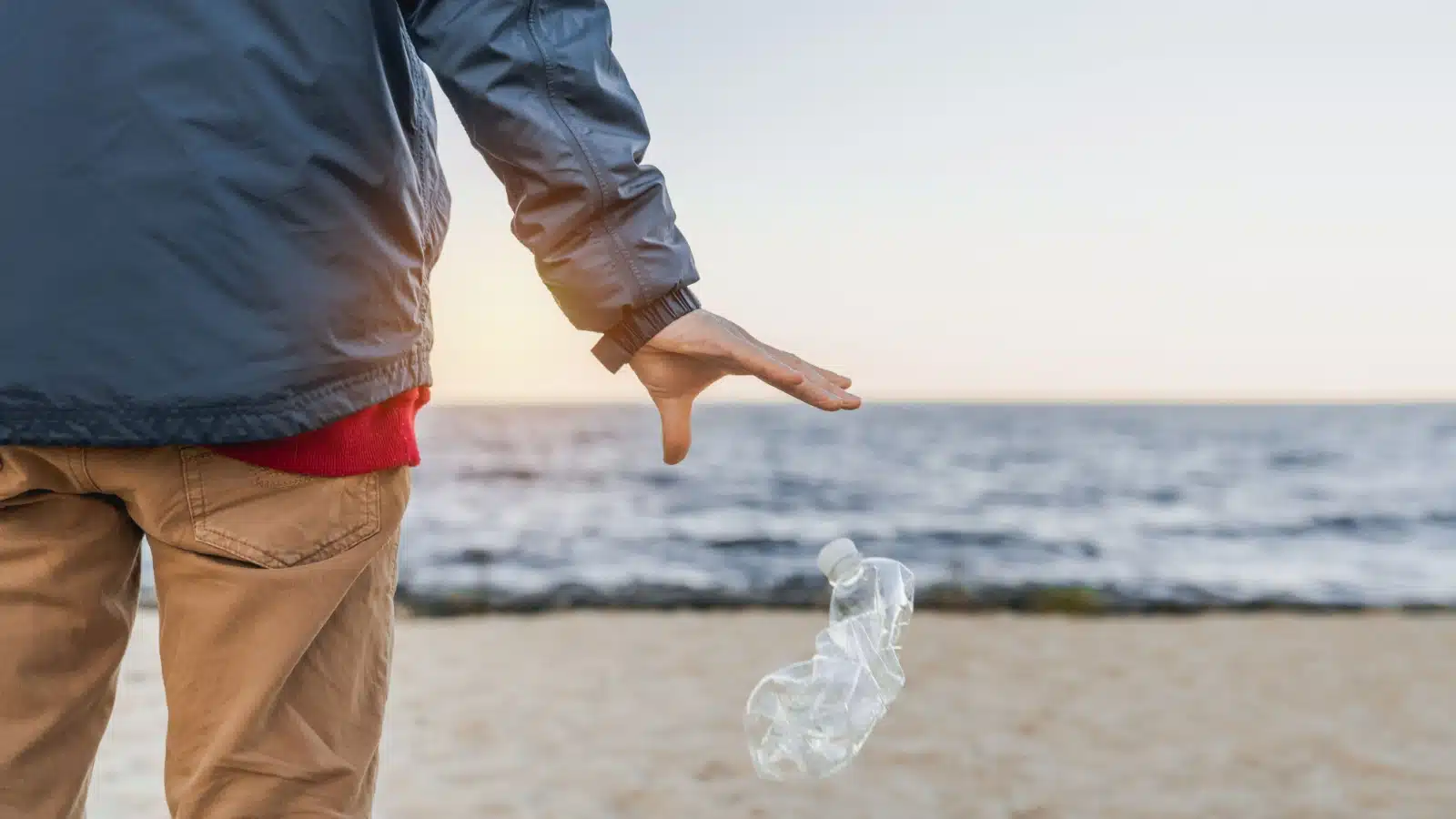A man litters on the beach by dropping his empty water bottle to the ground.