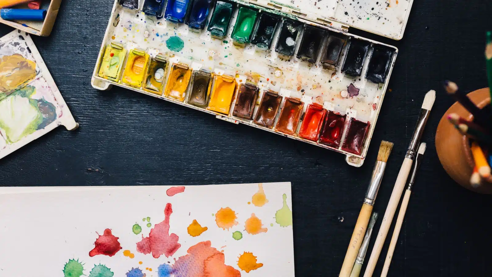 An art table with messy watercolors and drops of watercolor painting on the art paper.