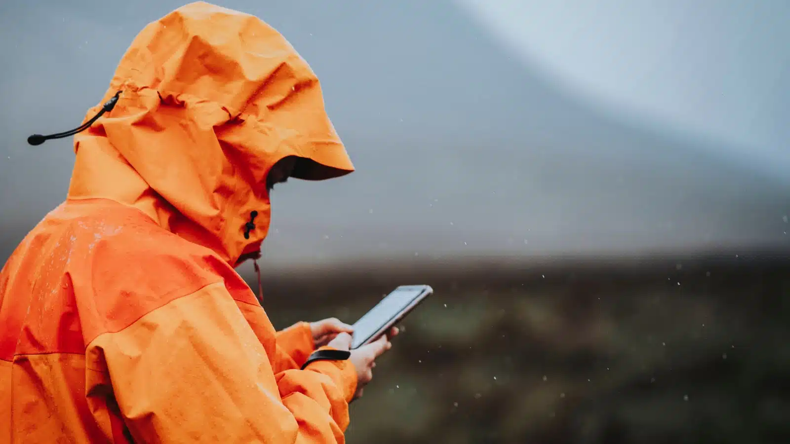 A person in a giant raincoat uses their cellphone in the rain