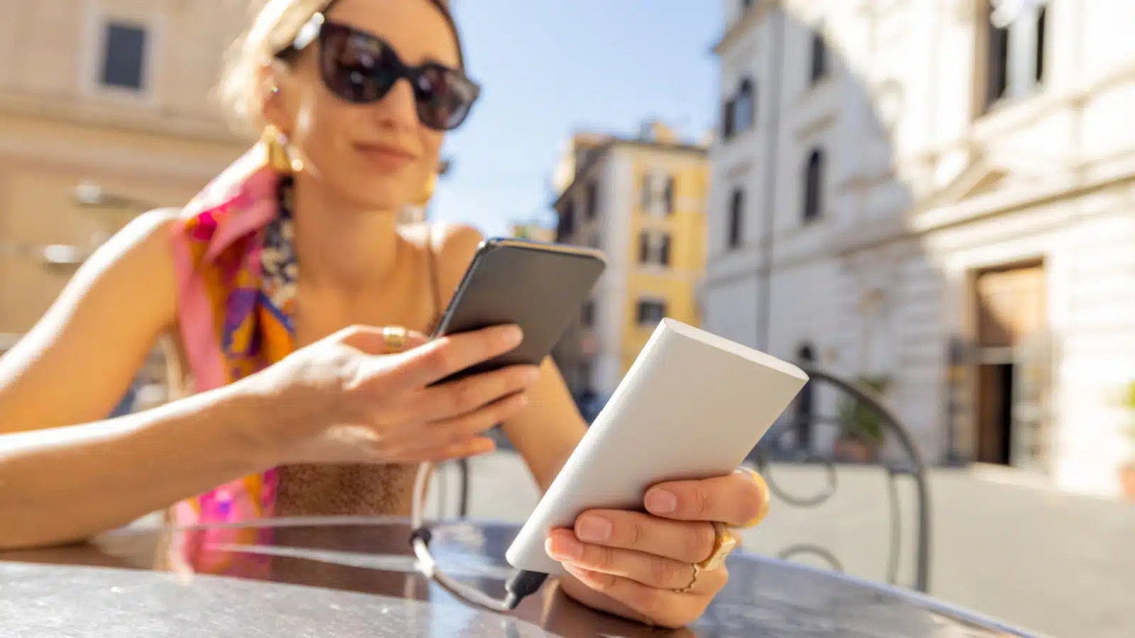 A woman charging her cell phone with a portable power bank at a cafe while traveling.